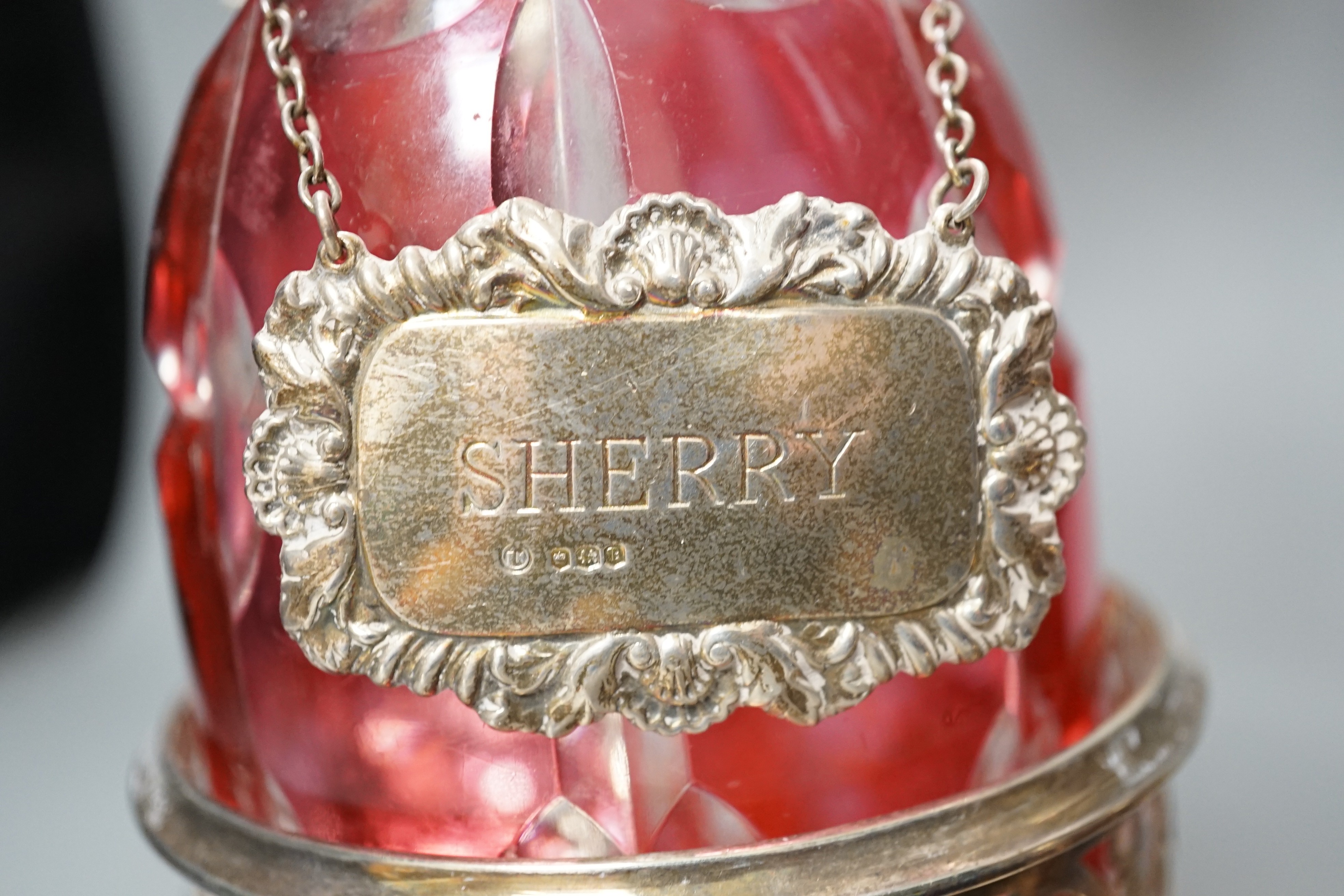 A pair of silver plated two branch, two light candelabra and a pair of silver plated decanter coasters with two ruby flash glass decanters with plated wine labels.